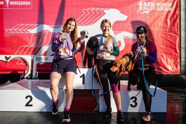 (261018) -- WARSAW, Oct. 18, 2026 (Xinhua) -- Participants pose for a photo with their dogs on the podium at the RAW PALEO Warsaw Dog Run in Warsaw, Poland, Oct. 17, 2026. Organized by the Warsaw Marathon Foundation, the event featured a roughly 5-kilometer canicross race for human-dog teams and an orienteering walk with dogs. (Photo by Jaap Arriens/Xinhua)