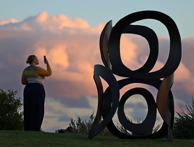 (261018) -- SYDNEY, Oct. 18, 2026 (Xinhua) -- A visitor takes photos of an exhibit at an outdoor exhibition at the seaside in Sydney, Australia, Oct. 17, 2026. Featuring sculptures by artists from Australia and across the world, the outdoor exhibition dubbed "Sculpture by the Sea" is held along the Bondi to Tamarama coastal walk in Sydney and will run until Nov. 2 this year. (Xinhua/Gong Bing)
