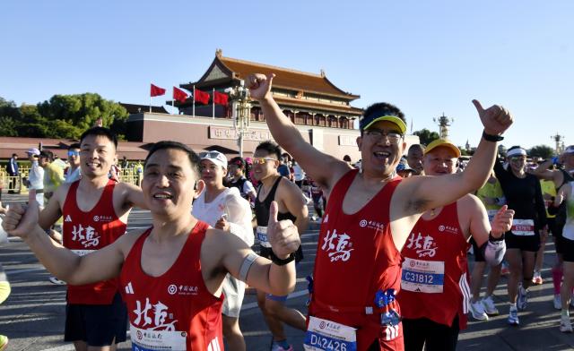(261018) -- BEIJING, Oct. 18, 2026 (Xinhua) -- Runners waves to cameras as they compete during the 2026 Beijing Marathon & National Marathon Championships in Beijing, capital of China, Oct. 18, 2026. (Xinhua/Li Xin)