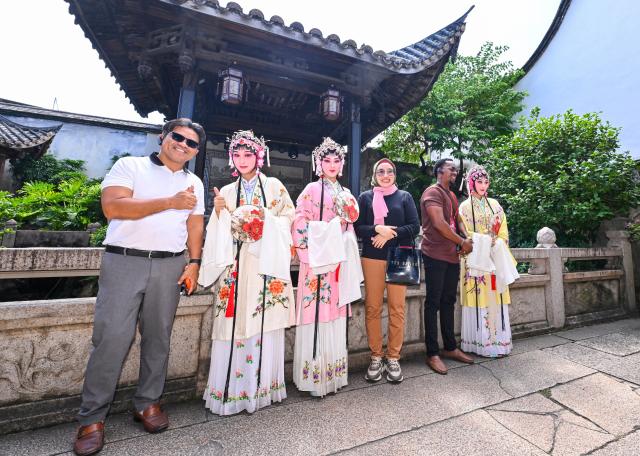 (261018) -- FUZHOU, Oct. 18, 2026 (Xinhua) -- Guests attending the 21st Century Maritime Silk Road Local Government Cooperation and International Friendship Cities Dialogue pose for photos with Minju Opera performers at the Three Lanes and Seven Alleys in Fuzhou, southeast China's Fujian Province, Oct. 18, 2026. Guests attending the dialogue made a tour in Fuzhou on Sunday. (Xinhua/Jiang Kehong)