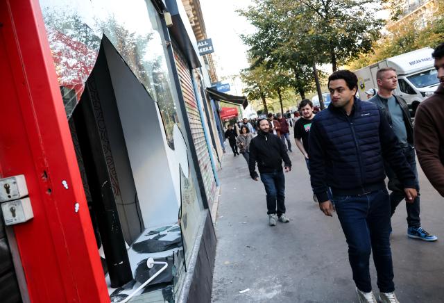(261019) -- BEIJING, Oct. 19, 2026 (Xinhua) -- People walk past a shop damaged during a protest in Paris, France, Oct. 18, 2026. French President Emmanuel Macron on Sunday vowed legal action against those responsible for violence during protests across the country on Saturday. (Xinhua/Wu Huiwo)