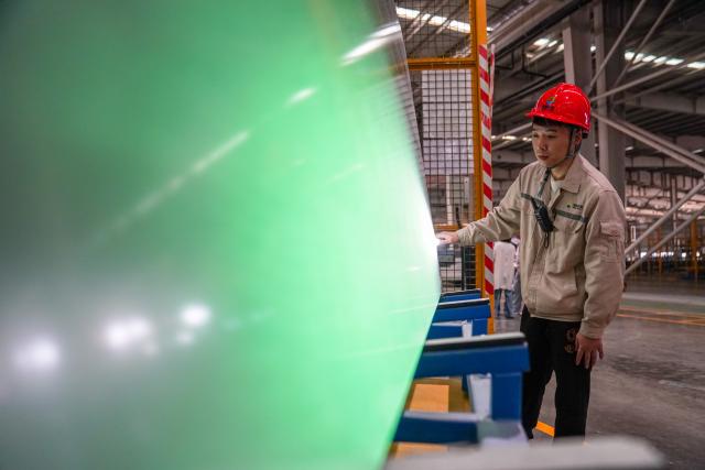(261020) -- ZHAOTONG, Oct. 20, 2026 (Xinhua) -- A staff member checks the quality of photovoltaic glass products in the workshop of Zhaotong Kibing Photovoltaic Technology Co,. Ltd. in Zhaotong City, southwest China's Yunnan Province, on Oct. 19, 2026. Leveraging its advantages in rich resources of silicon ore and the development of green electricity, Zhaotong City has attracted leading enterprises to develop the photovoltaic glass manufacturing industry, bringing about employment for surrounding residents. Currently, the city has basically formed an industrial chain from silicon mining and washing to the manufacturing of photovoltaic glass and photovoltaic modules. (Xinhua/Peng Yikai)