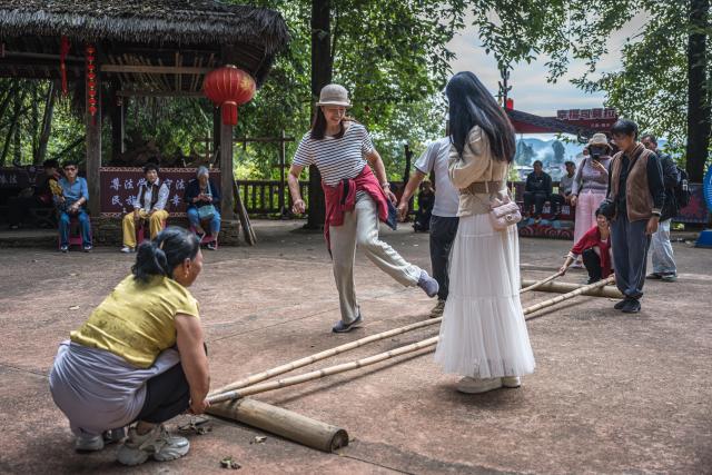 (261020) -- TENGCHONG, Oct. 20, 2026 (Xinhua) -- Tourists experience bamboo-stick dance in Simola Wa Village in Qingshui Town of Tengchong City, southwest China's Yunnan Province, Oct. 19, 2026. The Simola Wa Village has a history of over 500 years and is home to people of multiple ethnic groups including the Wa, Han, Bai and Dai. Simola means "a place of happiness" in the Wa language. In recent years, the village has relied on its ethnic cultural resources to create a distinctive cultural tourism industry, attracting a continuous stream of tourists. (Xinhua/Wang Guansen)