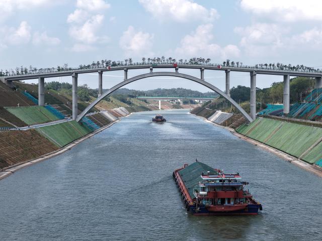 (261021) -- QINZHOU, Oct. 21, 2026 (Xinhua) -- An aerial drone photo taken on Oct. 21, 2026 shows cargo vessels passing through the dedicated wildlife corridor bridge over the Pinglu Canal in south China's Guangxi Zhuang Autonomous Region. Cargo throughput of the Pinglu Canal has surpassed 1 million tonnes since its opening to navigation on Sept. 16.
  The 134.2-kilometer canal runs from Nanning, capital of south China's Guangxi Zhuang Autonomous Region, to the Beibu Gulf, the closest maritime outlet for much of southwest China.
  The canal stretches along the New International Land-Sea Trade Corridor, a strategic trade route connecting China's inland regions with ASEAN and other global markets. It is the first river-to-sea canal project planned and coordinated at the national level since the founding of the People's Republic of China in 1949. (Xinhua/Zhou Hua)