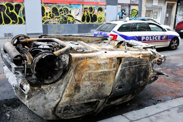 (261021) -- PARIS, Oct. 21, 2026 (Xinhua) -- A police vehicle drives past a vehicle destroyed by fire during the earlier demonstration on a street in Paris, France, Oct. 21, 2026. The French government has vowed to do everything within its power to prevent violence at fresh social demonstrations announced for Saturday, after riots around the country caused widespread destruction and thousands of arrests on Oct. 17. (Xinhua/Wu Huiwo)