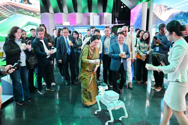 (261023) -- XIONG'AN, Oct. 23, 2026 (Xinhua) -- Participants of the 2026 Global Governance Forum (Xiong'an) interact with a robot dog while visiting a smart-city science and innovation center in Xiong'an New Area, north China's Hebei Province, Oct. 23, 2026. The 2026 Global Governance Forum (Xiong'an) kicked off here on Friday and will last till Sunday. Participants from various countries and regions visited a smart-city science and innovation center and the construction site of the start-up zone of Xiong'an New Area ahead of the forum. (Xinhua/Mu Yu)
