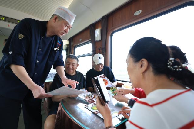 (261024) -- HARBIN, Oct. 24, 2026 (Xinhua) -- A staff member introduces delicacies served aboard the train Z114/111 on Oct. 22, 2026.
  The train Z114/111, running between Harbin in northeast China's Heilongjiang Province and Haikou in south China's Hainan Province, has witnessed a surge of passengers before winter arrives in Heilongjiang.
  The train service, which takes about 48 hours to finish the 4,300-km-long journey, is popular among elderly travelers from northeast China heading south to escape the bitter winter cold. (Photo by Xu Shuai/Xinhua)