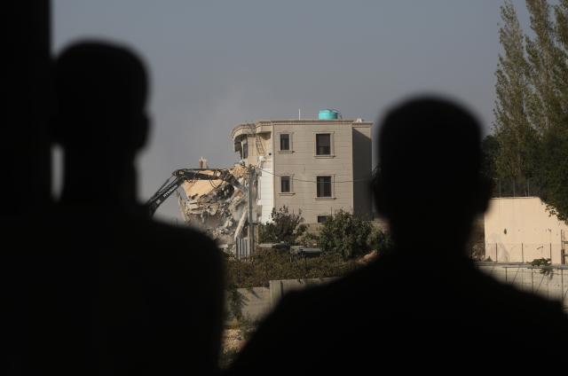 (261024) -- HEBRON, Oct. 24, 2026 (Xinhua) -- People watch a bulldozer demolishing a residential building near the northern entrance of the West Bank city of Hebron, on Oct. 23, 2026. Israel is preparing a major military operation in the West Bank, Israeli Prime Minister Benjamin Netanyahu said Friday, as local sources said Israeli forces demolished a residential building in Hebron and closed the city's main entrances following a shooting attack that killed two Israeli soldiers and two Palestinian attackers. (Photo by Mamoun Wazwaz/Xinhua)