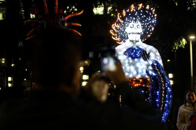 (261024) -- MEXICO CITY, Oct. 24, 2026 (Xinhua) -- A visitor takes photos of a Day of the Dead-themed light art installation along Paseo de la Reforma in Mexico City, capital of Mexico, Oct. 23, 2026. As the Day of the Dead approaches, giant light sculptures along Paseo de la Reforma in Mexico City, capital of Mexico, are illuminated. (Photo by Francisco Canedo/Xinhua)
