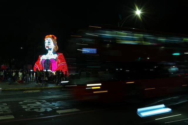 (261024) -- MEXICO CITY, Oct. 24, 2026 (Xinhua) -- A bus passes by a Catrina-shaped light art installation along Paseo de la Reforma in Mexico City, capital of Mexico, Oct. 23, 2026. As the Day of the Dead approaches, giant light sculptures along Paseo de la Reforma in Mexico City, capital of Mexico, are illuminated. (Photo by Francisco Canedo/Xinhua)