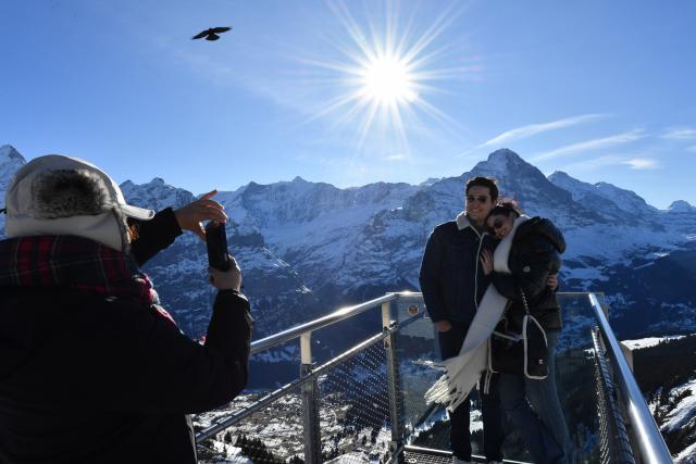 (261025) -- GENEVA, Oct. 25, 2026 (Xinhua) -- This file photo shows visitors posing for a photo with the background of the snow-covered mountain scenery on the First Cliff Walk at Grindelwald-First mountain in the canton of Bern, Switzerland, Dec. 18, 2025. TO GO WITH "Feature: Taste of China's Wuyi Mountain at Switzerland's Grindelwald-First" (Xinhua/Lian Yi)