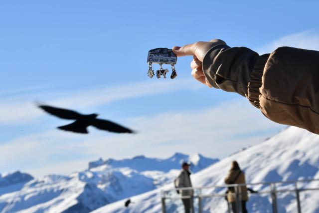 (261025) -- GENEVA, Oct. 25, 2026 (Xinhua) -- This file photo shows a tourist displaying a souvenir with the background of the snow-covered mountain scenery at Grindelwald-First mountain in the canton of Bern, Switzerland, Dec. 18, 2025. TO GO WITH "Feature: Taste of China's Wuyi Mountain at Switzerland's Grindelwald-First" (Xinhua/Lian Yi)