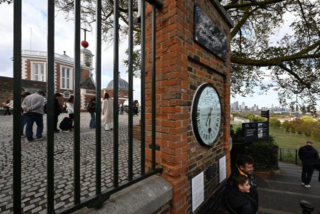 (261025) -- LONDON, Oct. 25, 2026 (Xinhua) -- Visitors pose for photos with the Shepherd Gate Clock at the entrance to the Royal Observatory in Greenwich, London, Britain, on Oct. 25, 2026. The clock was the world's first to display Greenwich Mean Time (GMT) directly to the public and features a 24-hour dial. Britain ended British Summer Time (BST) at 2am on Sunday, October 25, 2026, setting clocks back one hour to Greenwich Mean Time (GMT). (Xinhua/Li Mangmang)