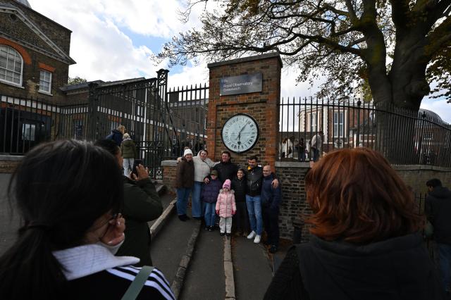 (261025) -- LONDON, Oct. 25, 2026 (Xinhua) -- Visitors pose for photos with the Shepherd Gate Clock at the entrance to the Royal Observatory in Greenwich, London, Britain, on Oct. 25, 2026. The clock was the world's first to display Greenwich Mean Time (GMT) directly to the public and features a 24-hour dial. Britain ended British Summer Time (BST) at 2am on Sunday, October 25, 2026, setting clocks back one hour to Greenwich Mean Time (GMT). (Xinhua/Li Mangmang)