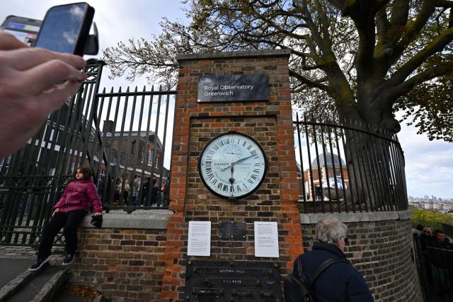 (261026) -- LONDON, Oct. 26, 2026 (Xinhua) -- Visitors view and photograph the Shepherd Gate Clock at the entrance to the Royal Observatory in Greenwich, London, Britain, on Oct. 25, 2026. The clock was the world's first to display Greenwich Mean Time (GMT) directly to the public and features a 24-hour dial. The Royal Observatory in Greenwich was founded in 1675 to improve navigation at sea through astronomical observations and help ships determine their longitude. As the home of Greenwich Mean Time, it holds an important place in the history of astronomy, precision timekeeping and navigation. In 1884, the meridian passing through the observatory was adopted as the international Prime Meridian, establishing a common reference for measuring longitude worldwide. This historic line is still marked at the observatory today. (Xinhua/Li Mangmang)