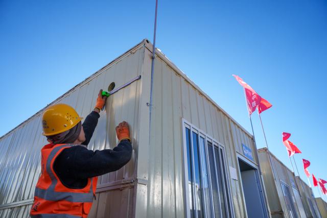 (261026) -- BAQEN, Oct. 26, 2026 (Xinhua) -- A worker of China Railway Group Limited drills a hole for chimney installation outside a prefabricated house at a resettlement site of a quake-hit village in Maru Township of Baqen County, Nagqu City, southwest China's Xizang Autonomous Region, Oct. 25, 2026.
  The first 60 prefabricated housing units in the earthquake zone were completed at 2:10 a.m. on Oct. 25, and electricity was connected to the units by 8 p.m. on the same day. (Xinhua/Gaesang Namgyae)