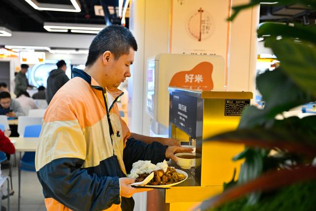 (261026) -- NANJING, Oct. 26, 2026 (Xinhua) -- A customer takes a bowl of soup from a machine at the AI Mirror World Restaurant in Nanjing, east China's Jiangsu Province, Oct. 26, 2026. With a human-machine collaborative operation model, the restaurant makes some of its meals and drinks through standardized production powered by AI kitchen equipped with smart noodle and beverage making machines. (Xinhua/Ji Chunpeng)