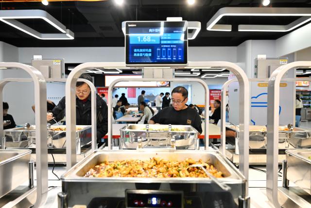 (261026) -- NANJING, Oct. 26, 2026 (Xinhua) -- People pick up their meals at the AI Mirror World Restaurant in Nanjing, east China's Jiangsu Province, Oct. 26, 2026. With a human-machine collaborative operation model, the restaurant makes some of its meals and drinks through standardized production powered by AI kitchen equipped with smart noodle and beverage making machines. (Xinhua/Ji Chunpeng)