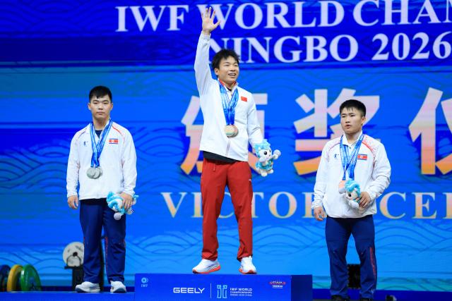 (261027) -- NINGBO, Oct. 27, 2026 (Xinhua) -- Total gold medalist Yang Yang (C) of China, total silver medalist Pang Un Chol (L) of the Democratic People's Republic of Korea (DPRK) and total bronze medalist Pak In Song of the Democratic People's Republic of Korea (DPRK) react during the awarding cermeony for the men's 60kg competition at the 2026 IWF World Championships in Ningbo, east China's Zhejiang Province, Oct. 27, 2026. (Xinhua/Jiang Han)