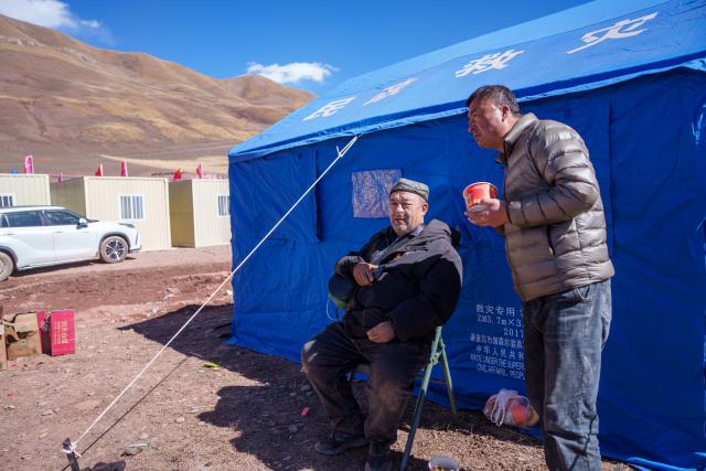 (261027) -- BAQEN, Oct. 27, 2026 (Xinhua) -- Alimjan Haliq (L) inhales oxygen at a temporary shelter in Maru Township of Baqen County, Nagqu City, southwest China's Xizang Autonomous Region, Oct. 26, 2026.
  In the wake of the earthquake that struck Baqen County on Oct. 22, several volunteers rushed to the quake-affected zone to serve hot meals, sending warmth to those affected who are facing high-altitude cold in late October.
   Among them was Alimjan Haliq, a volunteer from northwest China's Xinjiang. Knowing how difficult it is to cook at high altitude, he brought two pressure cookers with him all the way to the quake zone. Zhe Jiaxin, a young woman from Xinjiang, spent nearly 48 hours on a bumpy journey through multiple cities before finally reaching the epicenter. Abdu, who runs a Xinjiang restaurant in Lhasa, quickly rallied his friends, gathered supplies, and rushed to the disaster area. Their paths were different, but they converged on the snow-covered plateau for the same purpose.
   "There is strength in numbers," Alimjan Haliq said, voicing the thoughts of every volunteer. Upon arriving in the quake zone, the rows of tidy tents and prefab houses, ample supplies, and locals helping one another deeply moved the volunteers. Zhe Jiaxin said with emotion, "I want to do all I can to help the children here feel more comfortable."
   The unceasing cook fires and hot food from the volunteers did more than fill empty stomachs -- they let the affected people feel be cared and supported. (Xinhua/Tenzin Nyida)