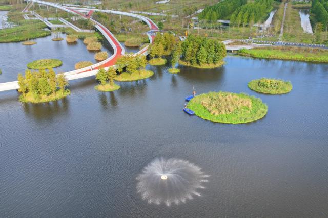 (261028) -- RUDONG, Oct. 28, 2026 (Xinhua) -- An aerial drone photo taken on Oct. 27, 2026 shows workers weeding on a floating island of Heming Park in Rudong County of Nantong City, east China's Jiangsu Province. In recent years, Rudong County in Nantong City has made efforts to improve its aquatic ecological environment. Water environment of the three rivers, namely the Taiyun River, the Jueju River and the Juekan River, which run through the county, has undergone sound remediation. Along these waterways, the Heming Park and the bank areas of tributaries have all formed a picturesque urban landscape for people to enjoy their leisure time. (Photo by Xu Congjun/Xinhua)