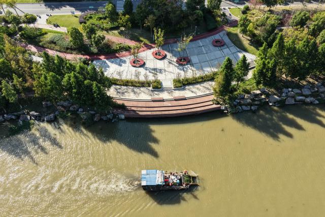 (261028) -- RUDONG, Oct. 28, 2026 (Xinhua) -- An aerial drone photo taken on Oct. 27, 2026 shows workers removing aquatic plants on the Jueju River in Rudong County of Nantong City, east China's Jiangsu Province. In recent years, Rudong County in Nantong City has made efforts to improve its aquatic ecological environment. Water environment of the three rivers, namely the Taiyun River, the Jueju River and the Juekan River, which run through the county, has undergone sound remediation. Along these waterways, the Heming Park and the bank areas of tributaries have all formed a picturesque urban landscape for people to enjoy their leisure time. (Xinhua/Ji Chunpeng)