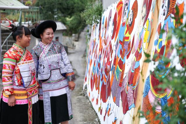 (261028) -- LIUPANSHUI, Oct. 28, 2026 (Xinhua) -- Luo Banmei (R), a farmer painter, looks at farmers' paintings on a wall with her daughter in Doujing Village of Shuicheng District in Liupanshui, southwest China's Guizhou Province, Oct. 5, 2026. In recent years, Shuicheng District has promoted its local art by offering painting training courses, establishing copyright trading platforms, and boosting the development of cultural and creative products.
   Shuicheng farmers' paintings are known for their bright, vibrant colors and exaggerated forms. These paintings bearing witness to local changes have become a cultural driver for rural revitalization. Since 2021, Shuicheng farmers' paintings have been exhibited in more than 20 countries and regions, including Britain, Japan and Australia. (Xinhua/Yang Wenbin)