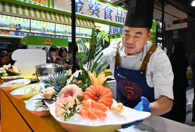 (261028) -- QINGDAO, Oct. 28, 2026 (Xinhua) -- A chef arranges exhibits at a booth at the 29th China Fisheries & Seafood Expo in Qingdao, east China's Shandong Province, Oct. 28, 2026. The expo kicked off here on Wednesday, with an exhibition area of approximately 120,000 square meters, showcasing exhibits covering aquatic raw materials and processed products, aquaculture and processing technologies and equipment, and cold chain logistics facilities. The expo, which will last until Oct. 30, has attracted numerous domestic and international manufacturers and buyers to seek business opportunities. (Xinhua/Li Ziheng)