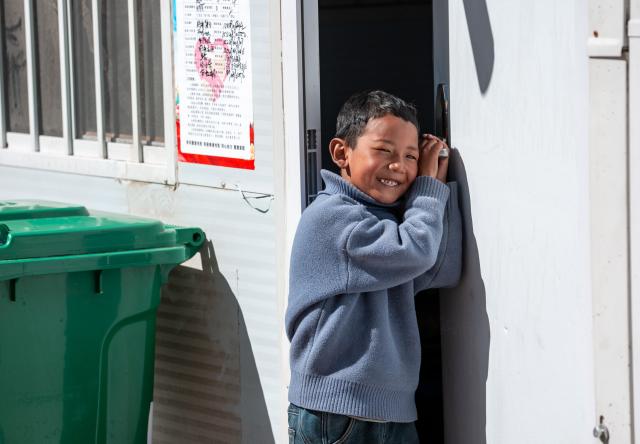 (261028) -- BAQEN, Oct. 28, 2026 (Xinhua) -- A child is pictured at the doorway of a prefabricated house at a resettlement site of a quake-hit village in Maru Township of Baqen County, Nagqu City, southwest China's Xizang Autonomous Region, on Oct. 28, 2026. A 7.0-magnitude earthquake had struck Baqen County in southwest China's Xizang Autonomous Region on Oct. 22. Days after the quake, villagers from Baqen County have started moving into prefabricated houses which rescue workers had rushed against the clock to build in the wake of the quake, and steadily restored their life order. (Xinhua/Tenzin Nyida)