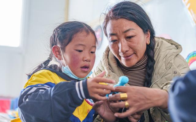 (261030) -- BAQEN, Oct. 30, 2026 (Xinhua) -- A child makes a handicraft under the guidance of a teacher at a makeshift kindergarten at a resettlement site of a quake-hit village in Maru Township of Baqen County, Nagqu City, southwest China's Xizang Autonomous Region, on Oct. 30, 2026. A makeshift kindergarten opened recently at a resettlement site here. Inside the comprehensively disinfected and carefully decorated facility, teachers are helping children from quake-hit villages adapt as soon as possible to learning and daily life at the resettlement site. (Xinhua/Gaesang Namgyae)