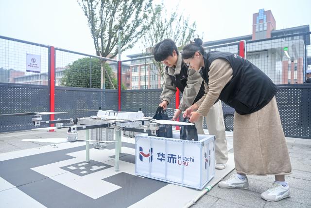 (261031) -- QINGZHEN, Oct. 31, 2026 (Xinhua) -- Staff members receive takeout food delivered by a drone in Guizhou Electronic Commerce Vocational College in Qingzhen vocational education town, Qingzhen City, southwest China's Guizhou Province, Oct. 30, 2026. Recently, the mountainous southwestern Chinese province of Guizhou has officially launched its first campus low-altitude drone delivery route in Qingzhen vocational education town. The aerial route connects local commercial districts directly to campuses, cutting the delivery time for teachers and students to less than 20 minutes with delivery fees starting at 3.8 yuan (about 0.57 U.S. dollars). The service also helps build a training platform integrating low-altitude industry and education to support talent cultivation. (Photo by Yuan Fuhong/Xinhua)